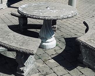 A PATINATED ANTIQUE STONE PATIO TABLE SET AND THREE BENCHES: Table Height 28.5 X Diameter 42 inches. Three Benches: Height 28.5 x Width 50 x Depth: 17 inches.
