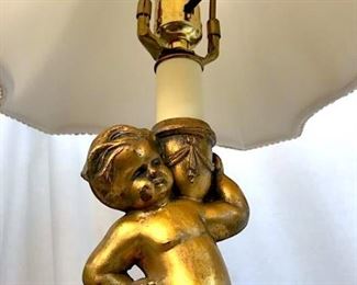 Pair of cherub putti Figural Table Lamps.  Coated material composite bases, possibly  resin, with gilt metal cherub figures  extending into single bulbs. Lot includes  lampshades and artichoke-form finials. Lampshade marked for Canterbury Roseart  Lampshades. Each measures approx 27 inches in  height by 13 inches in diameter with shades.  Lamps have not been tested. Interior home  decor lighting, cherub putti angel figural Lamps, Table Lamps, Light fixtures. 