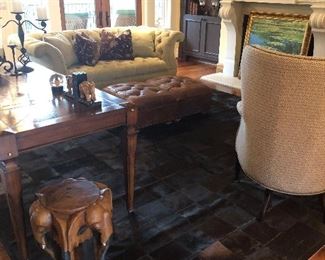 Overview of living room showing cow hide rug, custom sofa, elephant side table, and pair of tufted leather ottomans