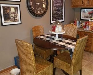 Gorgeous pedestal kitchen table with wicker weave chairs. NOTE: Big wall clock and two framed photos on wall are not for sale