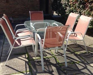 Glass and metal patio set with six orange mesh chairs.