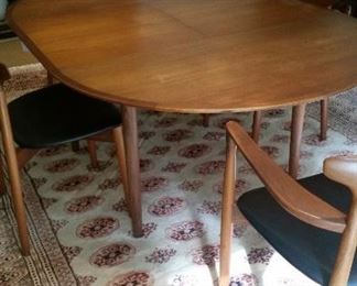 Danish Modern Teak dining table with 2 arm chairs & 3 side chairs. Centre leaf converts and folds neatly into storage below surface of table.