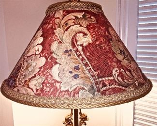 A floor lamp with rust and beige colors and a gold tone stand.