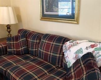 Sherrill plaid couch w/ 2 throw pillows, brass lamp & end table. Woven Christmas throw lays over one end of the couch. Elaine Bradley gold framed print hangs above couch. 