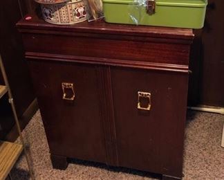 Kenmore sewing machine in a wooden cabinet w/ seat. Green sewing box, rabbit & duck shaped pillows, tin cans, cross-stitch sewing kit, cross-stitch sewing supplies & artificial flower arrangement.
