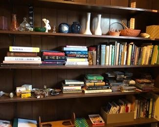 Bookcase filled with vases, books, cassette tapes, 2 brass picture easels, matches & other household ornaments.