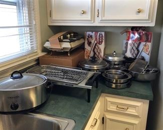 2 Brownie pans in boxes, stainless steel chaffing dish w/ 3 compartments, electric grill & frying pan, stainless steel bowls, pots, pans & frying basket & pressure cooker. Stainless steel crock pot holder.