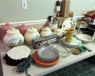 Set of pink ceramic canisters, set of beige ceramic canisters & matching utensil holder, new spring form pan w/ attachments, boxed stainless steel paper towel holder, cake stand, several ceramic plates &  bowl, pair of decorative ceramic handle utensils, glass casserole dish & other miscellaneous kitchen items.