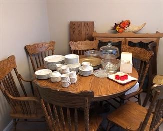 Noritake American Flowers dinnerware set, glass cake stand w/ lid, gold charger plates, crystal bowl on a silver stand, cloth napkins w/ rings, & cornucopia placed on an oak dining room table w/ extra extension leaf & six spindle back chairs. Behind the table is an oak hutch.