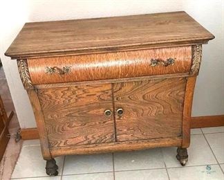 Antique Wood Sideboard on Casters	
Appears to be Oak, One drawer with Two Doors; Note the detail in the curvature of the wood doors and drawer; 34"w x 18"d x 31"h