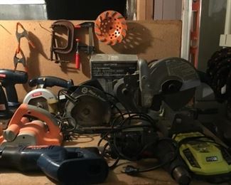 Black and Decker Circular Saw, Craftsman Auto Scroller Saw, Mikita 10in Miter Saw, Black and Decker Jig Saw, Ryobi 18 v One and Dual Chemistry Intelliport Charger. Background: Clamps and Diamond Saw Cutting Blade.