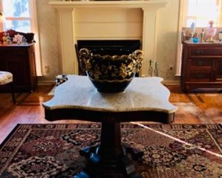 Antique French jardinière on early empire center hall table with antique wash stands in the back ground along with a mantle filled with unique antique items