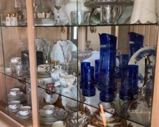 display space of a blond oak china cabinet display space, filled with antique glassware and china.  