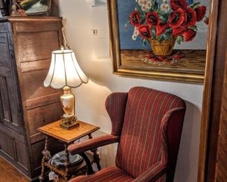 Unusual wool covered French wingback chair, unique side table with nicely turned, and unique legs. Vintage lamp, with large needlepoint floral wall art.