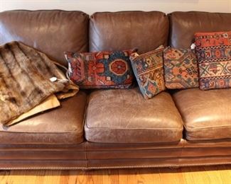 Brown leather sofa shown with throw pillows made from antique hand knotted Oriental rugs and fur throw.