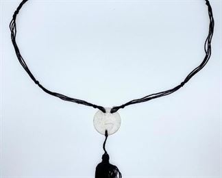 Renee Lalique glass pendant, medallion shape with nude figure attached with black silk woven tassle cord 1.25 in. diameter Condition: minor chip on back edge, otherwise good