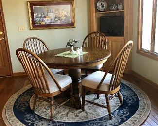 Round oak table and 4 curved back chairs. Round polyester rug, corner cabinet is built in and not for sale.