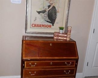 Living Room:  A slant-front drop leaf secretary over four drawers has a banded design and bracket feet.  Also shown is an authentic vintage French poster, leather books and a small faux plant.  Closer photos follow.