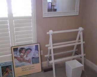 Bedroom #1-Main Floor:  A MARY CASSATT book and a MARY CASSATT framed poster are to the left of a white contemporary blanket rack, white wicker mirror and white waste can.
