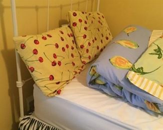 White iron twin bed with assorted bedding.