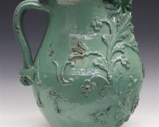 A Late 18th Century English Terracotta Jug. Hand thrown jug with green slip tin glaze, pinched spout, applied molded handle, floral motif, and date "1798" and initials "MV" about the exterior. Crazing, losses/flakes, loss to the "N" of "Anno". 13 1/2" high.