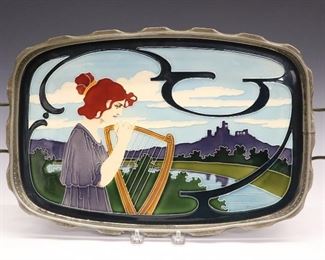 An Art Nouveau Johan Von Schwarz Enameled Ceramic Tray, Designed by Carl Sigmund Luber. Rounded rectangular tray set with enameled ceramic plaque that is decorated with the image of a Classical style woman with a harp, in the midst of a landscape, impressed "5098 CN" verso; set within a white metal frame with scalloped rim, pierced gallery and handles at either side, all resting on ball feet. Carl Sigmund Luber, German, 1896–1934. Wear to the metal, especially the finish, one handle is repaired, lacks one ball foot, and crazing. 18 3/4 x 11 3/8".