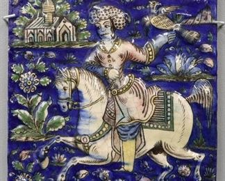 A Persian Glazed Ceramic Tile. Rectangular form with multi-colored decoration including vibrant blue, green, yellow, and pink which adorns the single scene of a falconer in which a man is shown riding a horse, holding a bird in his left hand, with a building in the distance. Purportedly from the Safavid Era, c.1501-1736. Crazing and some flakes/chipping at edges. 10 x 13 1/2" high.