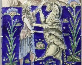 A Persian Glazed Ceramic Tile, dated 1319. Rectangular form depicting a man fighting a winged lion, with calligraphy above and below, decorated with polychrome glaze in azure, sky blue, green, white, and pink. Crazing evident, some chipping around edges, fine crack at upper left side. 15 3/4 x 22" high.
