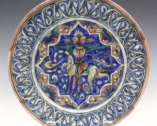 A Persian Ceramic Plate. Polychrome decoration with a foliate rim enclosing a central medallion with mythical beasts, in blue, green and pink on a white ground. Wear and heavy crazing with some roughness and tiny flakes at the rim. 8 1/2" diameter.