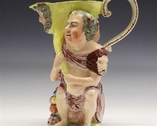 An early 19th century Staffordshire jug. Molded design with Bacchus seated in a wine cask, Pan with his pipes verso, a Satyr mask spout and scrolled handle with Polychrome decoration. Some surface wear, minor flaking at rear of base. 12 1/2" high.
