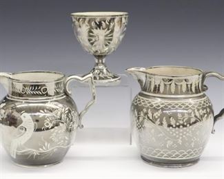 Three 19th century English Pearlware items with Silver lustre decoration, one footed cup and two jugs. All with flowers and foliage, one jug with Parrots. Wear, crazing, light surface scratches, minor spout flakes, one jug with crack at the foot rim. Up to 5 1/2" high.