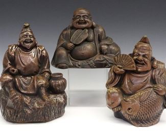Three Japanese Bizen Ware Figures. Brown pottery "Lucky god" figures include 1 figure of Hotei, shown seated with a fan, 2 figures of Eibisu, the god of plenty, one shown holding a fish and a fan, and the other shown seated beside a basket. Wear to the glaze, Hotei with a chip on the base, the larger Eibisu figure lacks an implement from his hand and has a chipped finger, minor wear to other piece. Up to 9" high.