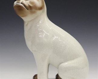 A Late 19th Century Galle Faience Dog. Figure of a seated dog, with glass eyes, creamy white body, and brow accents at the feet and head, with crackle glaze overall. Unmarked. Light wear to the painted decoration at the mouth, minor wear overall. 12" high.
