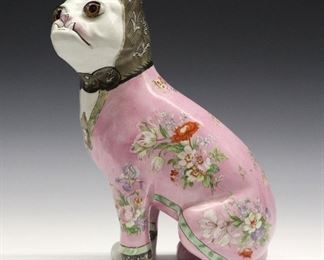 A Late 19th Century Galle Faience Dog. Figure of a seated dog, with glass eyes, is painted with ornate decoration consisting of a lily motif at the back of the head, a pink body with various floral sprays, and a collar with a locket suspended from it containing a portrait of a dog. Only marked with a black "F" in script is at the underside of one foot, and a red "H" at another. Light wear to the decoration, firing crack evident at the interior. 12" high.