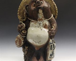 A Japanese Ceramic Sculpture of Tanuki. Glazed ceramic figure of the Folklore version of Tanuki, or a Raccoon Dog, shown wearing a hat and carrying a bottle. Open at the base and at the back of the figure's hat. Some small firing cracks, minor wear overall. 26" high.