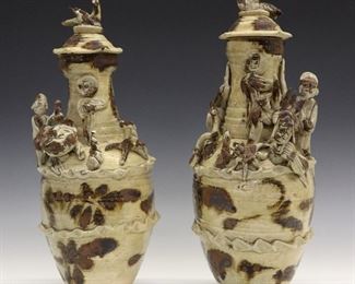 A Pair of Chinese Qingbai Glazed Hunpings (Funerary Covered Urns). Each baluster form with iron brown accents and applied decoration consisting of a dragon, a small figure and a bird on one and a tiger, small figure, and dog on the other; both with dome form covers, surmounted by bird form finials. Most likely from the late Southern Song (960-1279) or Yuan Dynasty (1279–1368). Some chips to each, one with repaired finial. 5 1/2" diameter, up to 14" high.