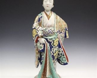 A Japanese Porcelain Meiji Period "Bijin" Figure. Polychrome enamel decorated porcelain figure of a beautiful young woman, dressed in an elaborate kimono with geometric and cherry blossom motifs with gilt accents overall. Unmarked. Head has been repaired, firing cracks at the underside and wear to gilt decoration. 18" high.