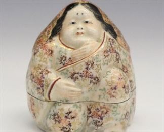 A Mid 19th Century Japanese Satsuma Porcelain Kogo, c.1850. Covered figural box in the form of a rotund Okame clothed in richly decorated clothes covered in patterns of scrolls and geometric motifs with gilt accents and crackle glaze overall. Signed at the underside in two lines, in red calligraphy. Light wear to the painted decoration, minor flake to the interior rim of the base. 3" high.