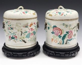 Two Chinese Porcelain Covered Jars. Each covered cylindrical vessel with loop handle at the top consists of a white ground that is decorated with gilt accents, pink flowers, leafy branches, peaches; bat and butterfly motifs with fine, twisted metal handles at either side. Unmarked. Some wear to the decoration, one with minute flaw to the rim of the cover, the other with a few small flakes to the rim. 7 3/4" high.