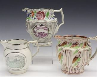 Three 19th century English Pearlware jugs with Pink/Silver lustre decoration. Two with paneled bodies and enamel decoration flowers and foliage and another with landscape vignettes. Wear, crazing, light surface scratches, the Pink/Green jug with a large crack at the side and staple repair at the handle, the other paneled jug with hairlines and a glued repair at the spout. Up to 6" high.