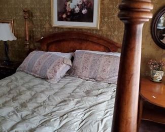 Queen size bed, picture on the wall, table to right, oval mirror, night stand and lamp.
