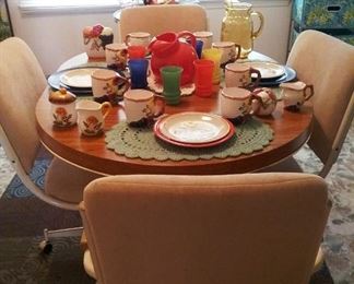 Vintage  dining room  set with upholstery on rollers. Vintage Fire King platonite beverage set in 50s bright primary colors.  Miscellaneous ceramic and plastic dishes on crocheted placemats. 