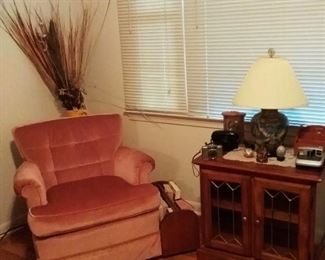 One of pair of vintage pink velvet  armchairs,  large painted urn with dried arrangement. One of pair of leaded glass fronted end tables with shelves. Vintage cameras as is and pottery  based  lamp.