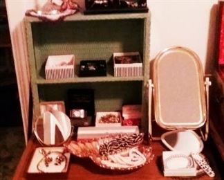 Green painted wicker bathroom shelves with inexpensive plastic clock musical jewelry box. Better boxed costume jewelry.  Rolling stand filled with  baskets of individual bagged jewelry and many watches.