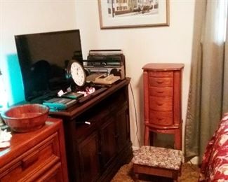 Her bedroom with flat screen tv and stand. Wooden veneered jewelry chest and small footstool with storage.