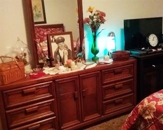 Double dresser with mirror,  Avon bottles, aquatic light, basket of sewing supplies, and miscellaneous artificial flower arrangements. 