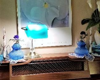 White flower artwork and desk lamp and upright wooden piano that looks like new