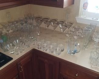 Kitchen is packed with glass , cooking,  flatware , dinner plates and more. 