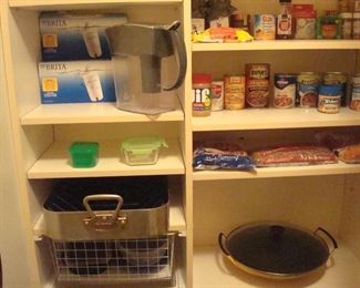 Kitchen Pantry-On Way to Garage:  A BRITA water pitcher and boxed filters are shown above a heavy duty ONEIDA roasting pan and rack, as well as some food items.  To the lower right is a yellow LeCREUSET wok.
