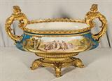 19th C. FRENCH PORCELAIN CENTER BOWL. BRONZE BASE. GILT PORCELAIN FIGURAL HANDLES. FIGURAL PANEL ON THE FRONT SIGNED A. CARRIER. P. C. LANDSCAPE PANEL ON THE BACK. 16" H X 24" W.